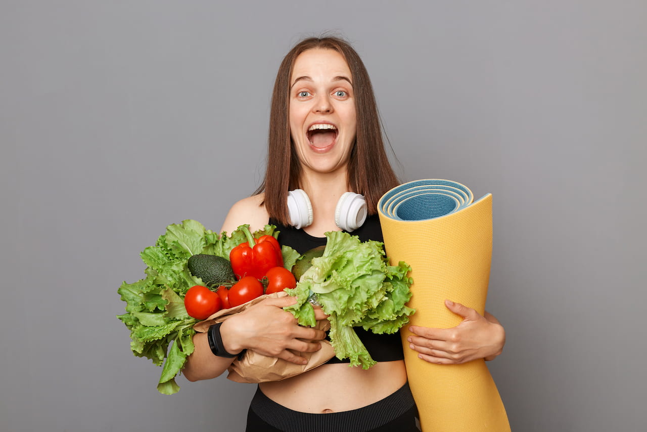 Спортивная девушка держит в руках овощи и коврик для йоги